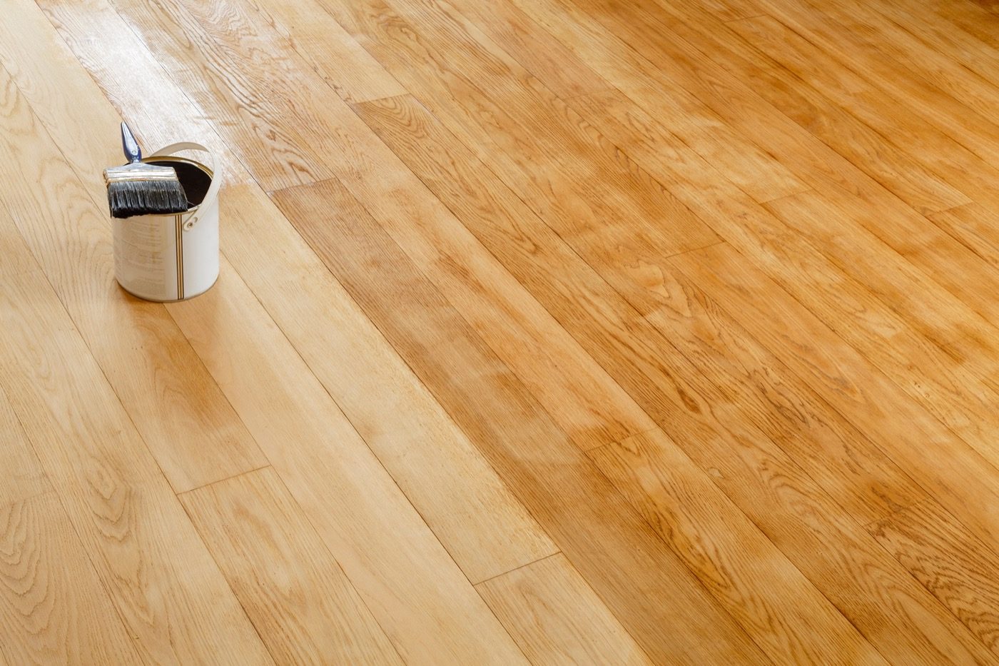 Barattolo aperto con pennello appoggiato su un parquet in rovere chiaro appena rifinito